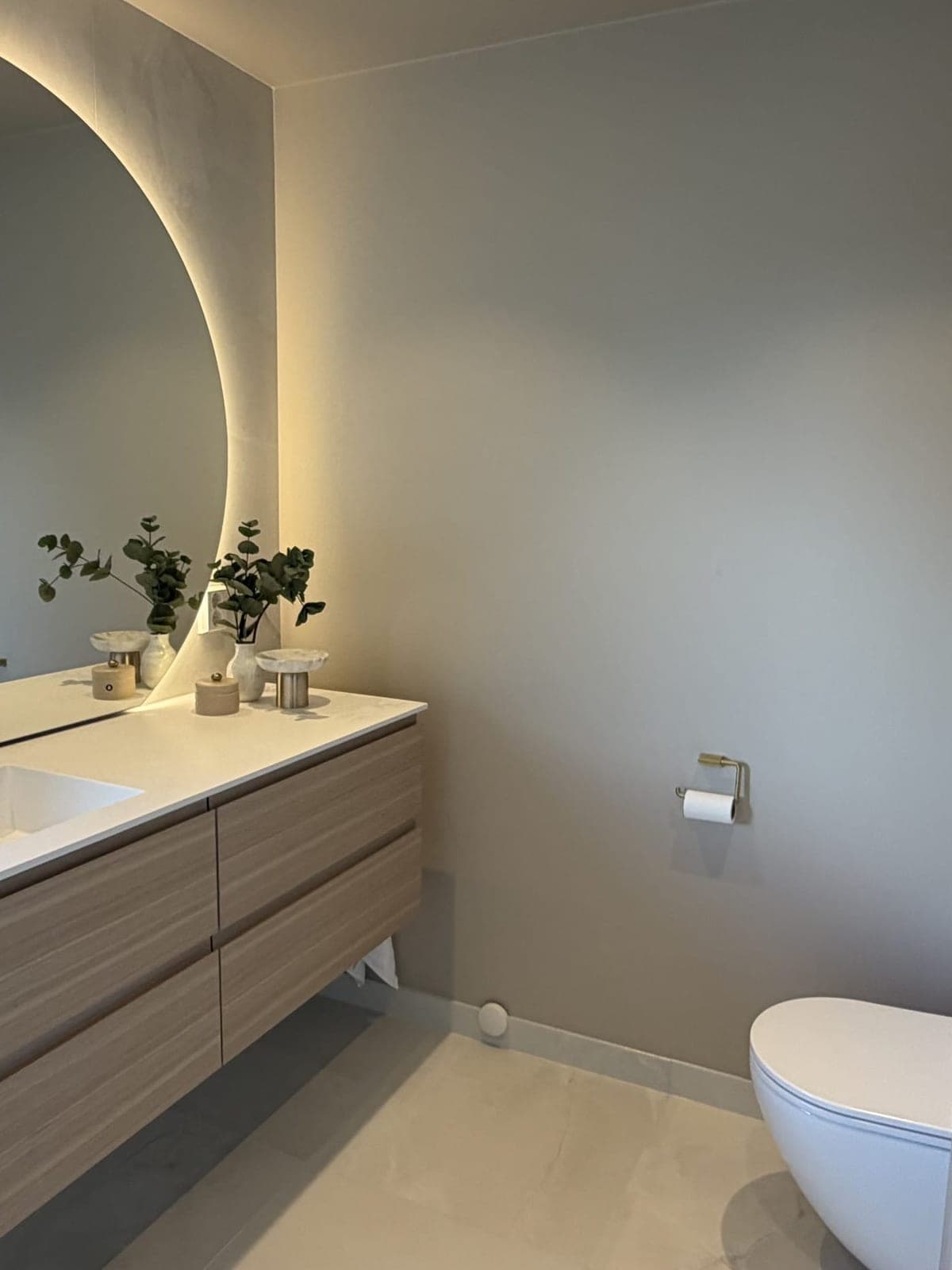 Servantvegg på badet på Austflata i Trondheim med lang servant, rundt speil med lys og vegghengt toalett